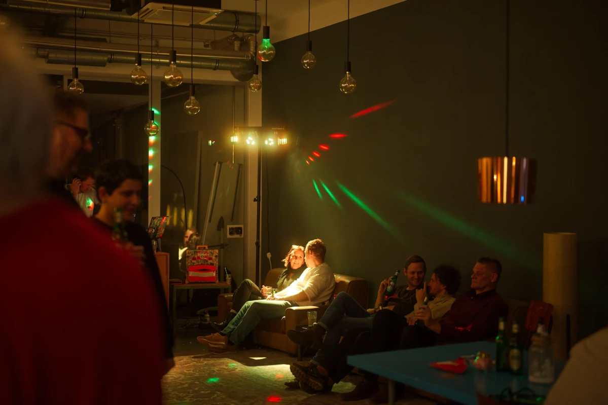 format h X-mas Party: Mitarbeitende auf Sofa und stehend bei Partybeleuchtung