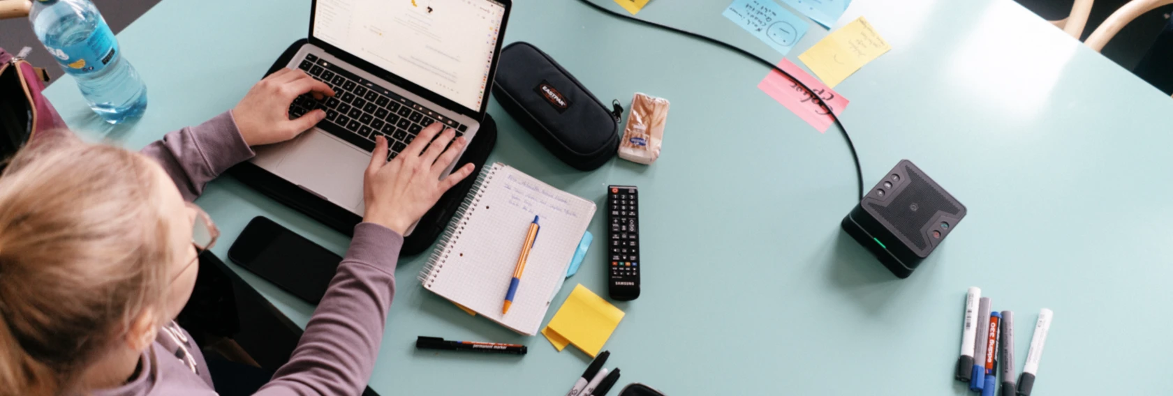 Flatlay Aufnahme: Software Developerin arbeitet am Laptop an größerem Meetingtisch